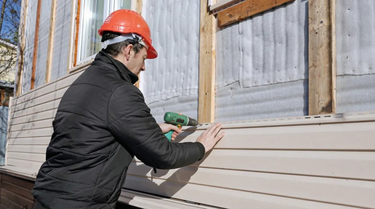 Siding replacement professional using a power drill to install new tan vinyl siding on a home exterior in Reno, NV